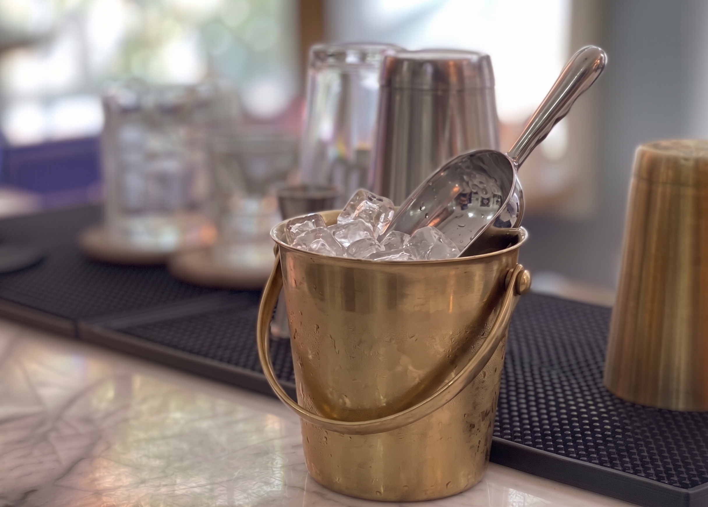 Cubitera metálica con hielo y pala, sobre una barra.