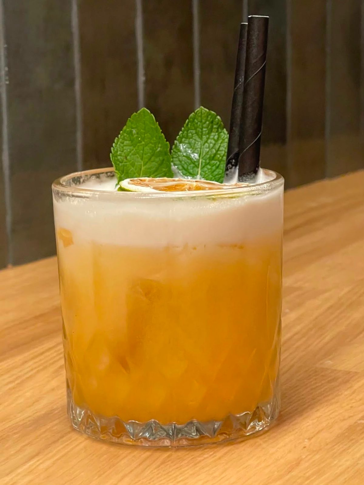 Vaso Old Fashioned con Amaretto Sour, espuma dorada, hojas de menta y una rodaja de cítrico.