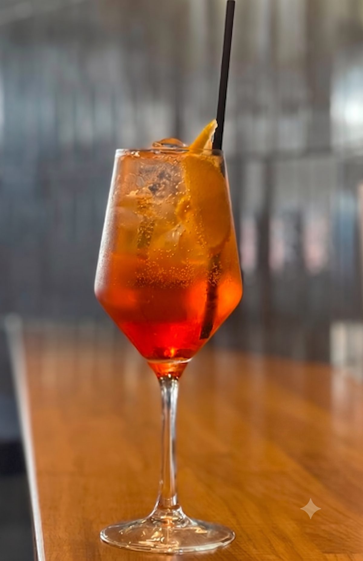 Copa de vino con Aperol Spritz de color naranja intenso, hielo y una rodaja de naranja.