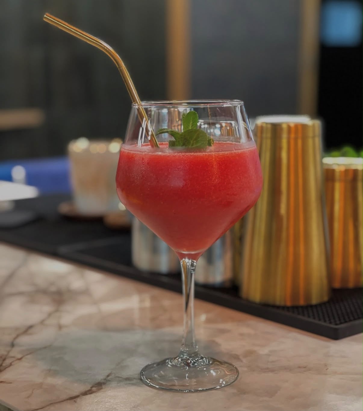 Copa balón con Frozen Daiquiri de fresa, pajita dorada y una ramita de menta.