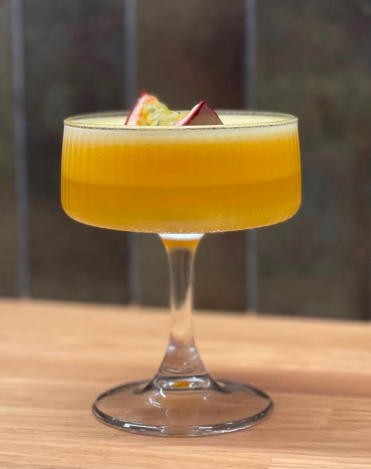 Copa coupe con Pornstar Martini de color amarillo anaranjado y fruta de la pasión flotando.