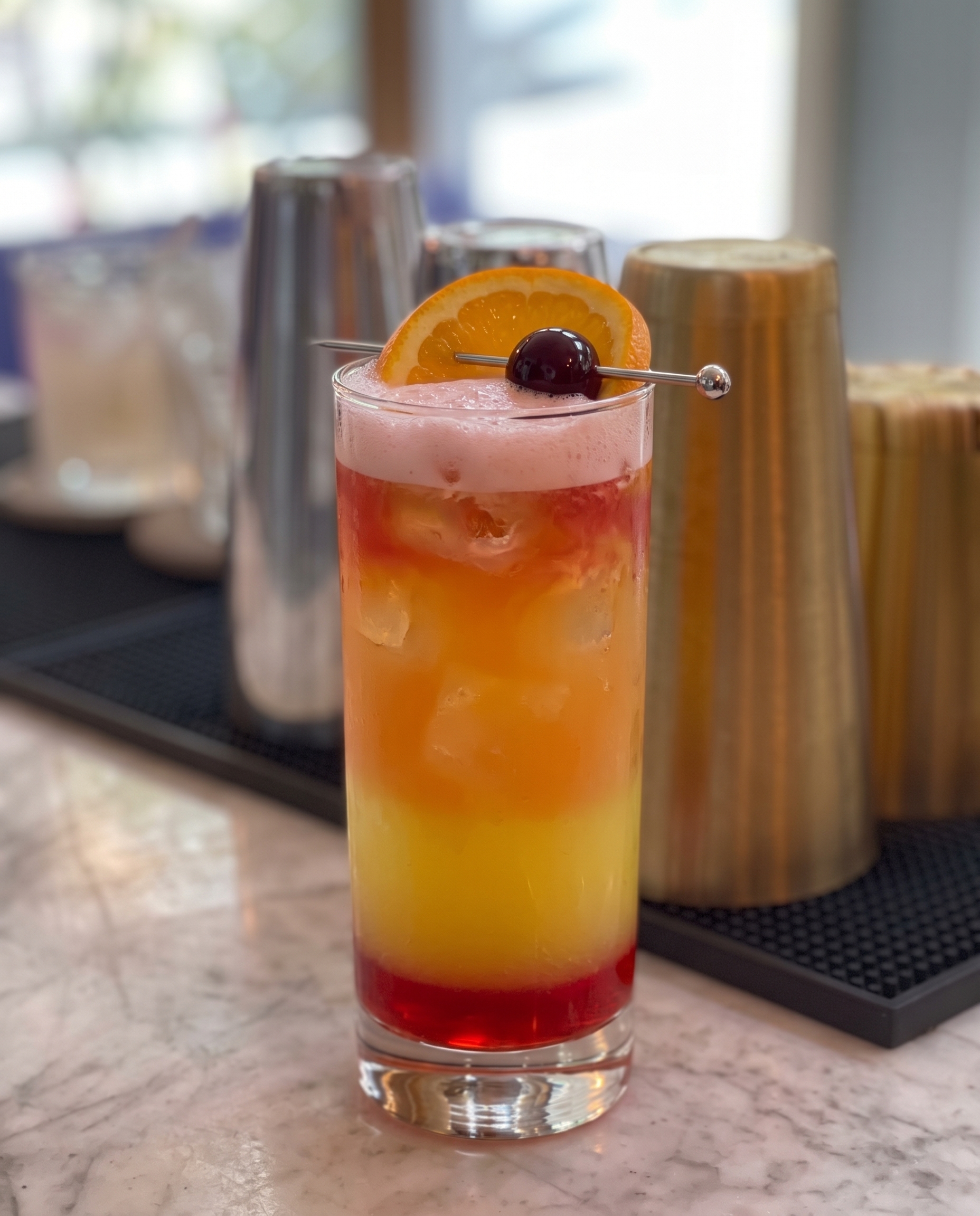 Vaso highball con cóctel San Francisco, de color naranja con degradado rojizo, hielo, rodaja de naranja y guinda en cóctel.