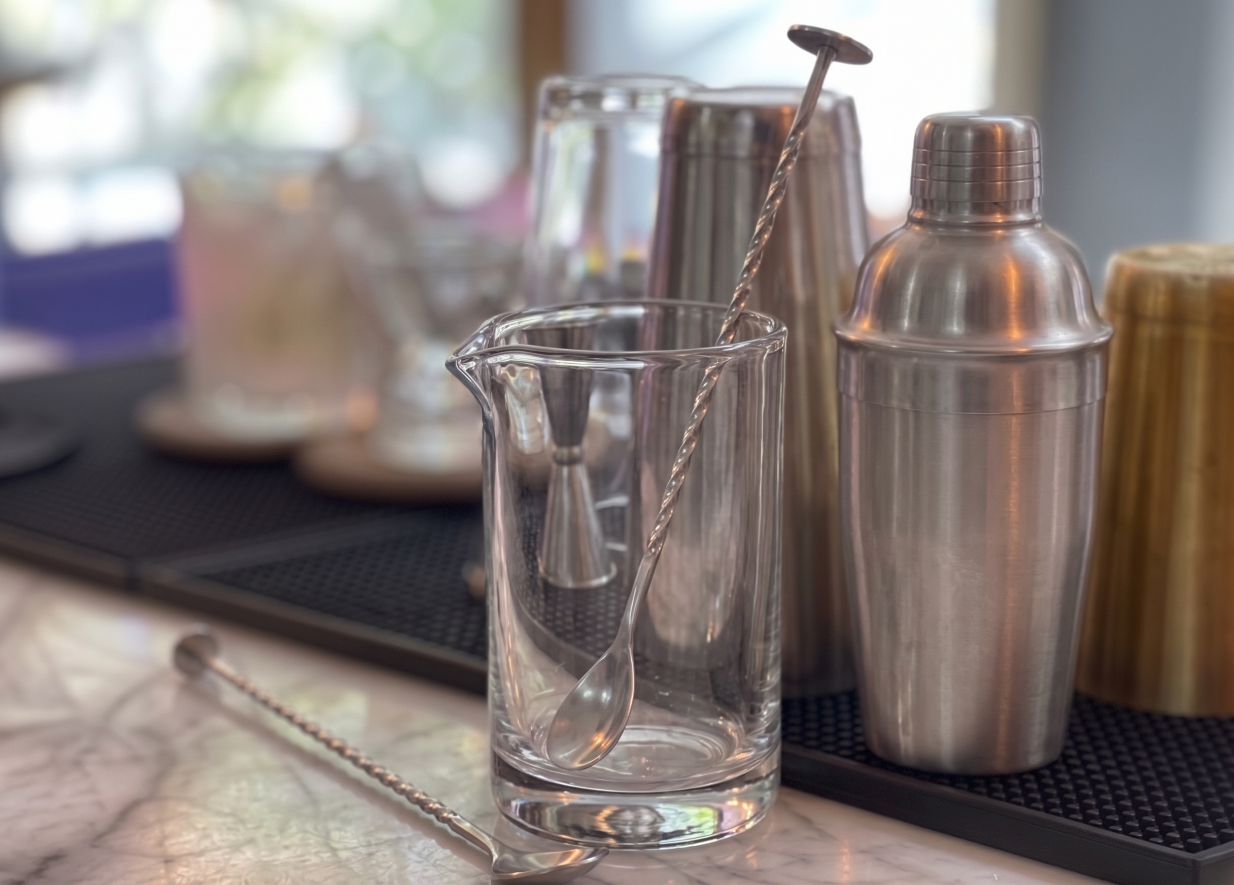 Vaso mezclador de cristal con cuchara de bar, sobre una barra.